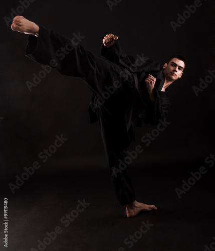 фотографія Studio portrait of young karate fighter kicking over black background