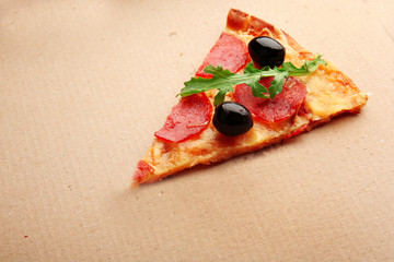 Slice of pepperoni pizza with arugula and olives on cardboard