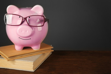 Wall Mural - Piggy bank with glasses and books on table ,gray background