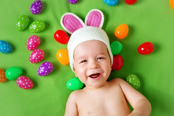 Wall Mural - Baby boy in bunny hat lying on green blanket with easter eggs