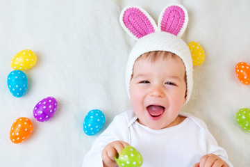 Wall Mural - Baby boy in bunny hat lying on green blanket with easter eggs