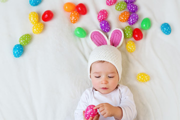 Wall Mural - Baby boy in bunny hat lying on green blanket with easter eggs