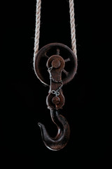 Big metal hook hanging on rope isolated on black background.