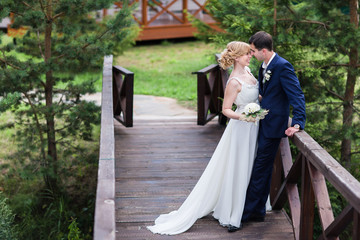 A happy young newly married couple walking in the park. Beautiful bride and groom kissing in the woods.