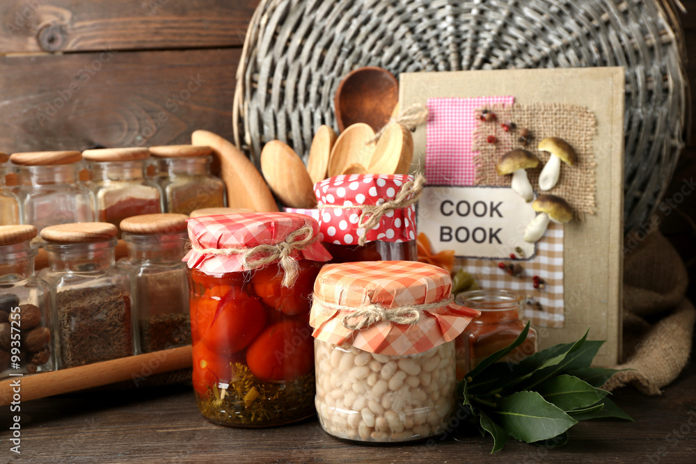 Jars with pickled vegetables, beans, spices and kitchenware on wooden background