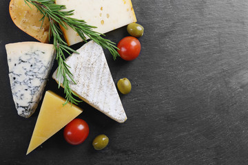 Wall Mural - Different kinds of cheese, tomatoes and olives on black board, copy space