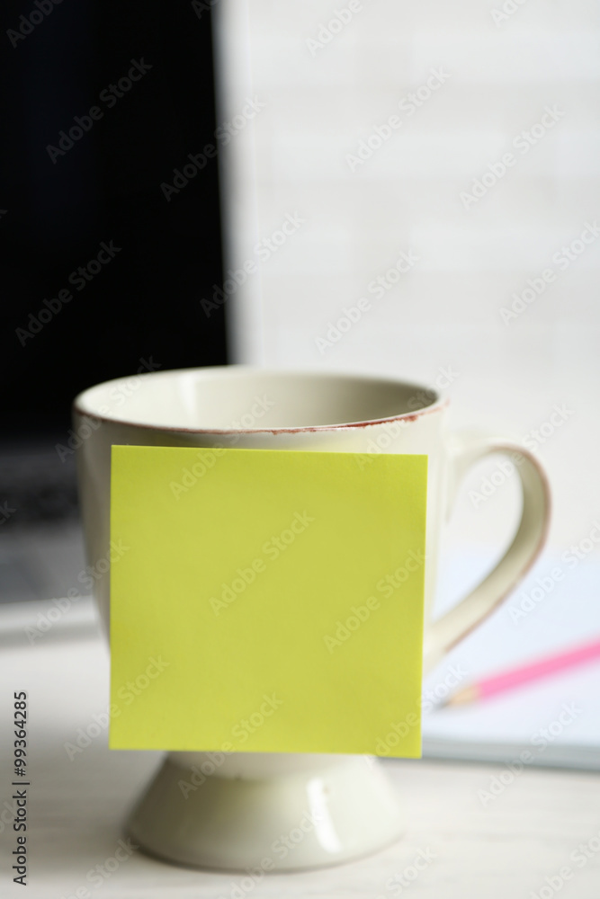 Yellow adhesive note on coffee cup, on laptop background