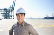 © Blue Jean Images - Male shipping industry worker with hands on hips with shipping dock background