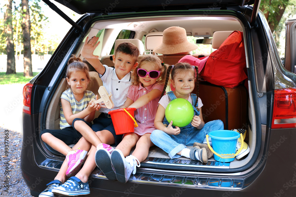 Three beautiful girls and boy sit on a car trunk and laughing