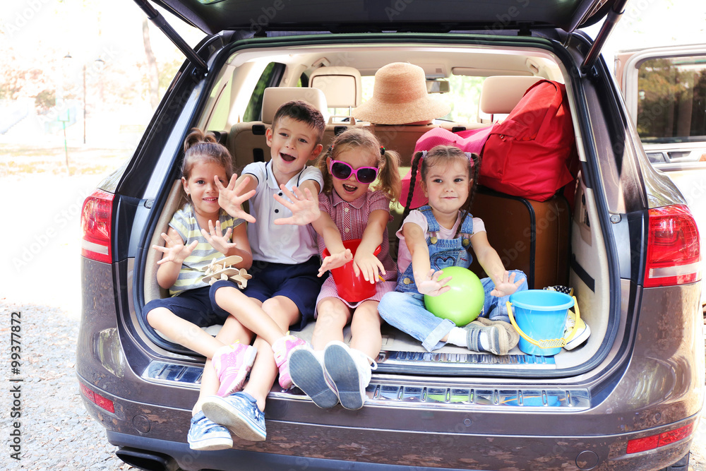 Three beautiful girls and boy sit on a car trunk and laughing