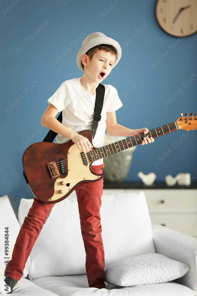 Little boy playing guitar ans singing on a sofa at home