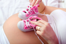Pregnant Mother Playing With Baby Sneakers While Lying In Bed