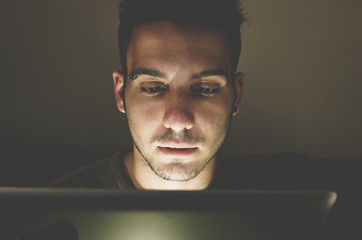 young handsome man at laptop computer with light reflection from the screen to the face - technology