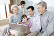 © Blue Jean Images - Grandparents and Parents with daughter look at Laptop on a sofa