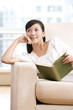© Blue Jean Images - Asian woman reading on a sofa