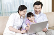© Blue Jean Images - Young couple and daughter look at laptop on sofa