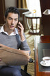 © Blue Jean Images - Young businessman reading newspaper and talking on phone