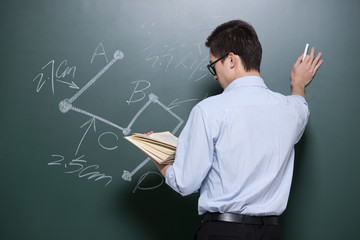 Professional male teacher writing on blackboard