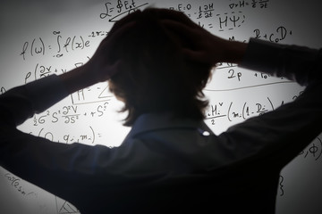Student holding his head looking at complex math formulas on whiteboard. Problem to solve