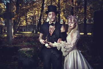 Dressed in wedding clothes romantic zombie couple walking on the abandoned cemetery.