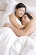 © Blue Jean Images - Asian couple cuddling on bed