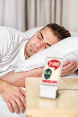 Wall Mural - Beautiful young man waking up with mobile alarm clock