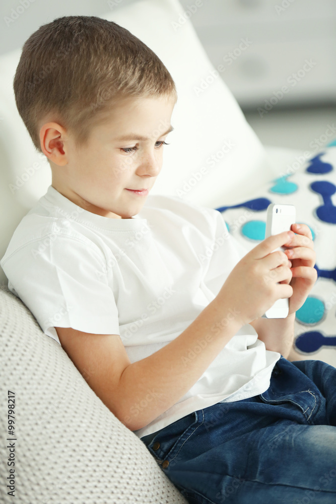 Little boy using mobile phone on a sofa at home