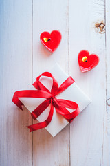 White box with red ribbon, red candles in the shape of heart. Romantic gift on Valentine's Day on wooden background.