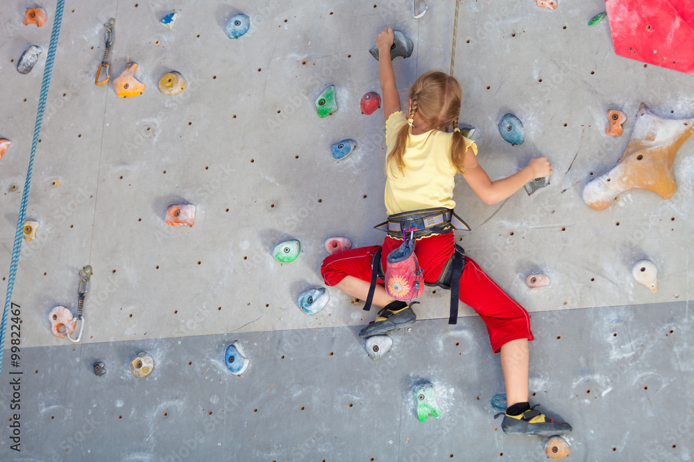 little girl climbing a rock wall - obrazy, fototapety, plakaty 