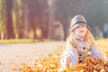 Wall Mural - Fun in leaves young blond girl in autumn day.