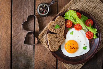 Breakfast on Valentine's Day - fried eggs and bread in the shape of a heart and fresh vegetables. Top view