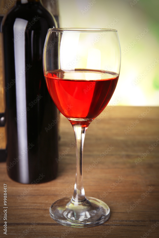 Red wine in glass and in bottle on blurred natural background