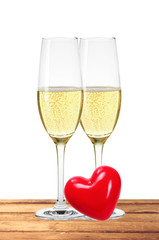 Two glasses of champagne and red heart on table isolated on whit