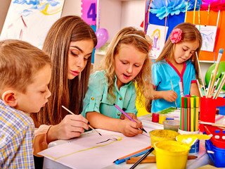 Wall Mural - Children with teacher woman learn painting on paper at table  in  kindergarten . 