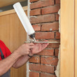 © sima - Worker installing wooden door, using polyurethane foam