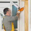 © sima - Worker installing wooden door, using polyurethane foam