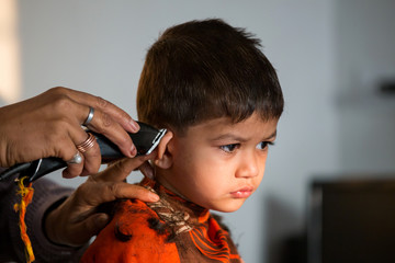 two year old kid having a haircut  with wet eyes after crying early morning with golden light falling on his face