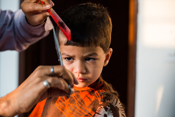 two year old kid having a haircut  with wet eyes after crying early morning with golden light falling on his face