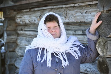 Wall Mural - The Russian woman in  shawl warms hands near an izba