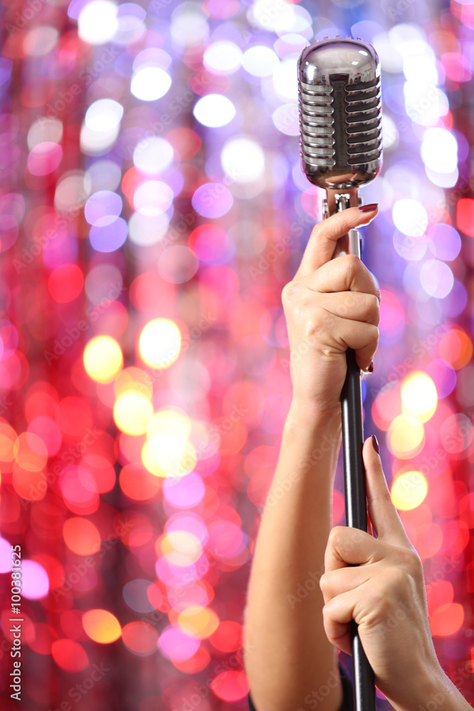 Female hands holding microphone against bright glitter background