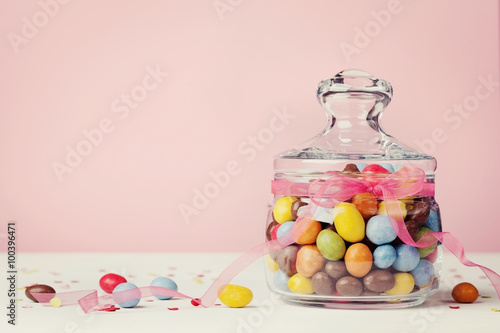 Colorful Candy Jar Decorated With Bow Ribbon Against Pink
