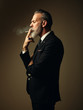 © SFIO CRACHO - Portrait of smoking gentleman wearing trendy suit and stands against the empty wall. Vertical