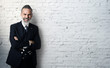 © SFIO CRACHO - Portrait of bearded businessman wearing trendy suit, stands against the brick white wall and smiling. Wide.