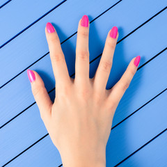 Female hand with pink nails on blue wooden background