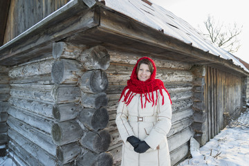 The Russian woman in  shawl warms hands near an izba