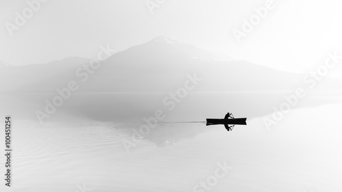 Zdjęcie XXL Mgła nad jeziorem. Sylwetka gór w tle. Mężczyzna pływa w łodzi z wiosłem. Czarny i biały
