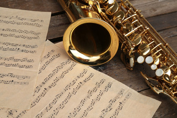 Wall Mural - Beautiful golden saxophone with musical notes on wooden background, close up