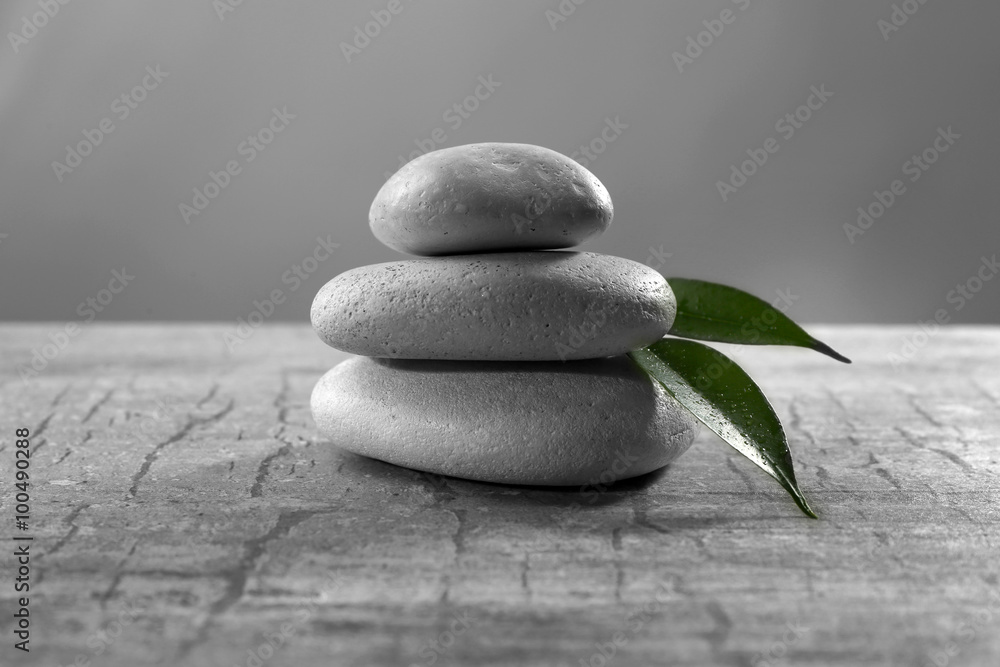 Pile of pebbles with leaf on the table against grey background