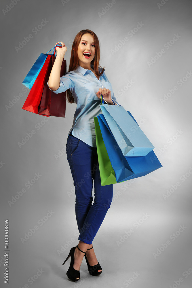 Young pretty woman with shopping packages on gray background