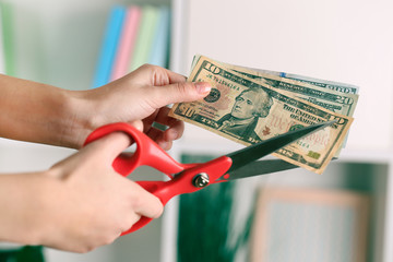 Poster - Hands with scissors cutting dollar banknotes, on blurred interior background